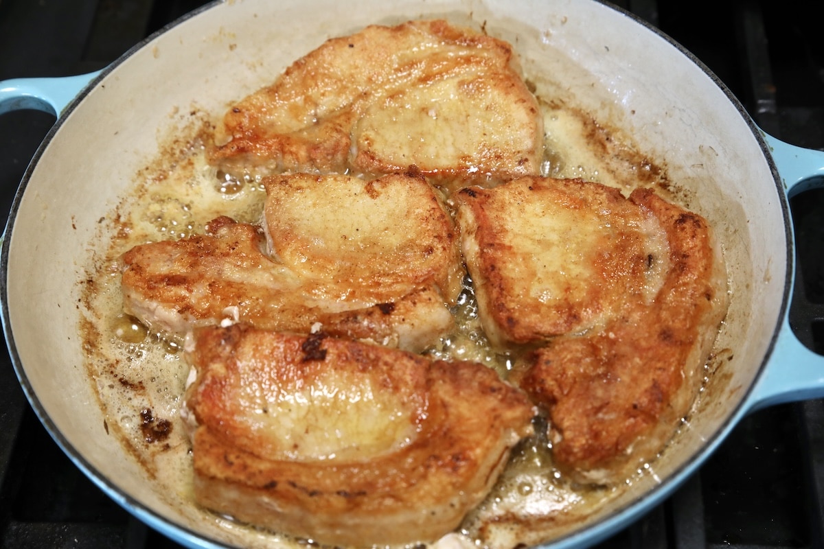 4 browned pork chops in a skillet.