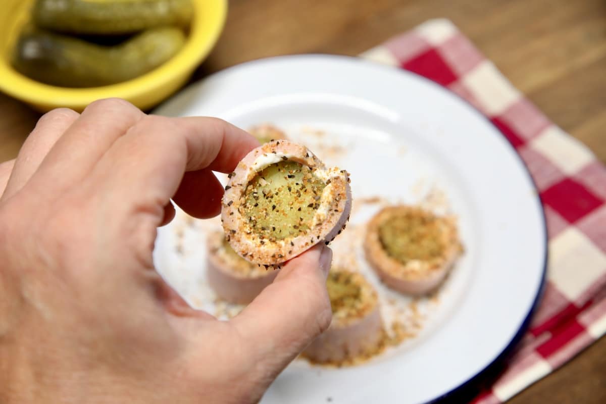 Hand holding bologna pickle roll up appetizer.