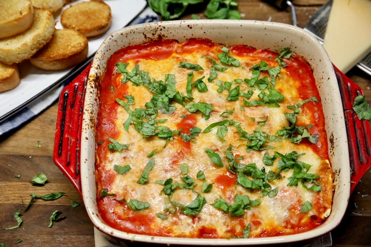 Casserole with ravioli and marinara, basil garnish.