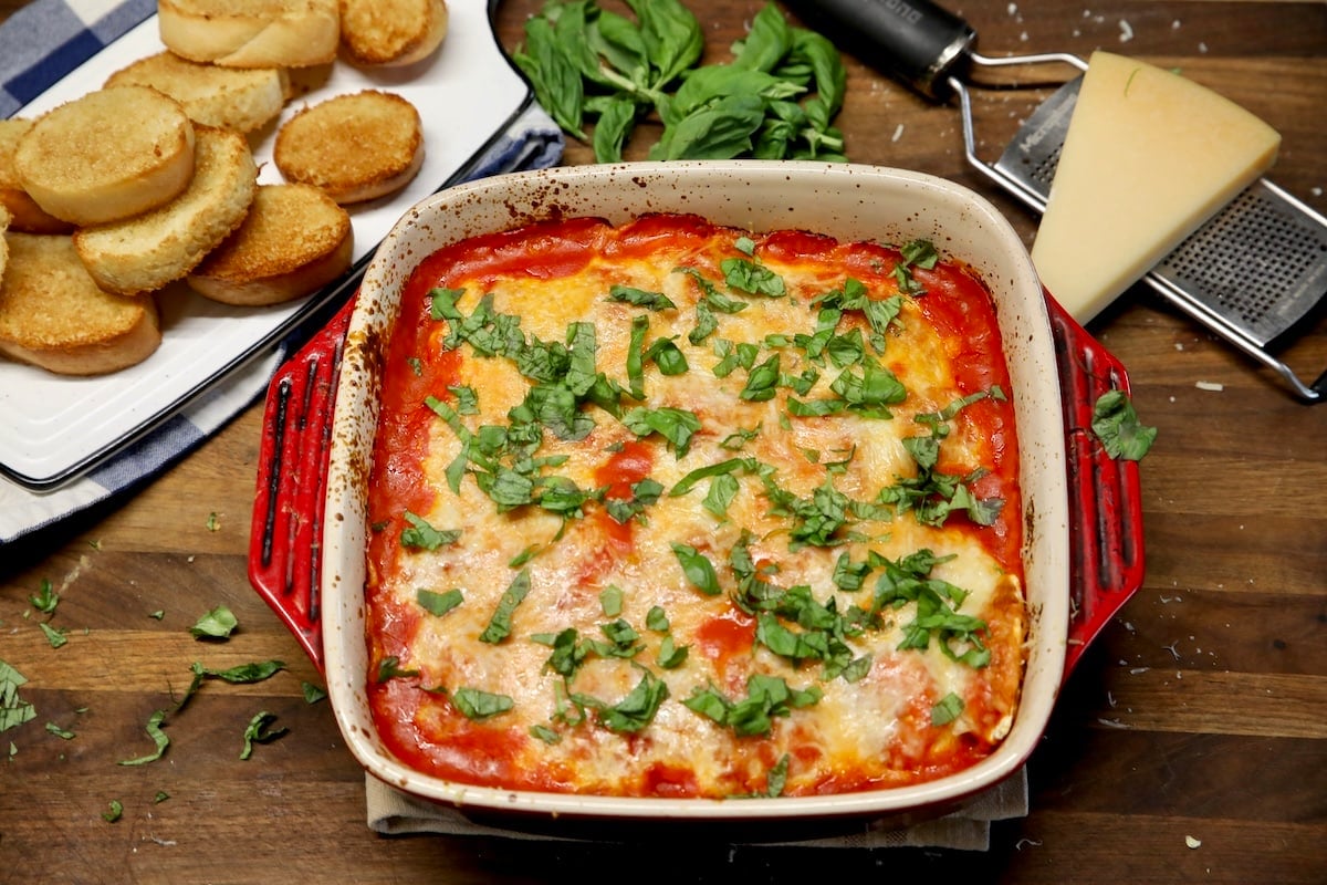 Easy lasagna casserole with ravioli. Pan of ravioli lasagna with tray of bread and wedge of parmesan cheese.