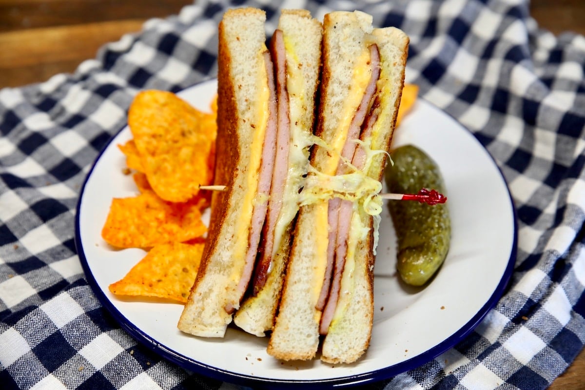 Sliced grilled cheese sandwich with bologna - pickle and chips on plate.