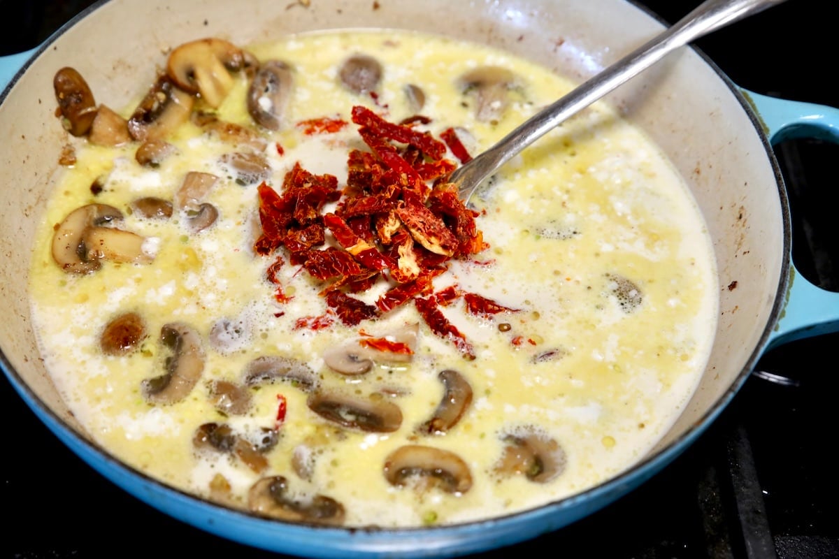 Making cream sauce for meatballs in a skillet with sun dried tomatoes.