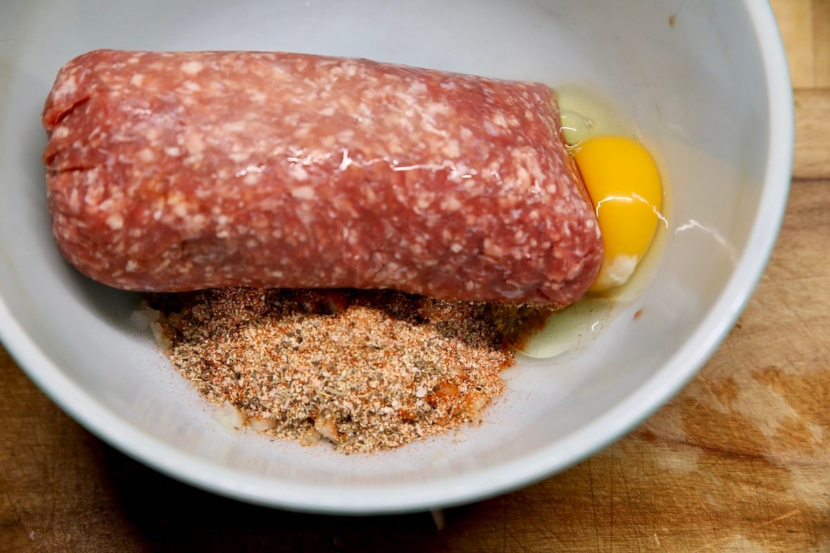 Bowl with ground beef, eggs, seasoning for meatballs.