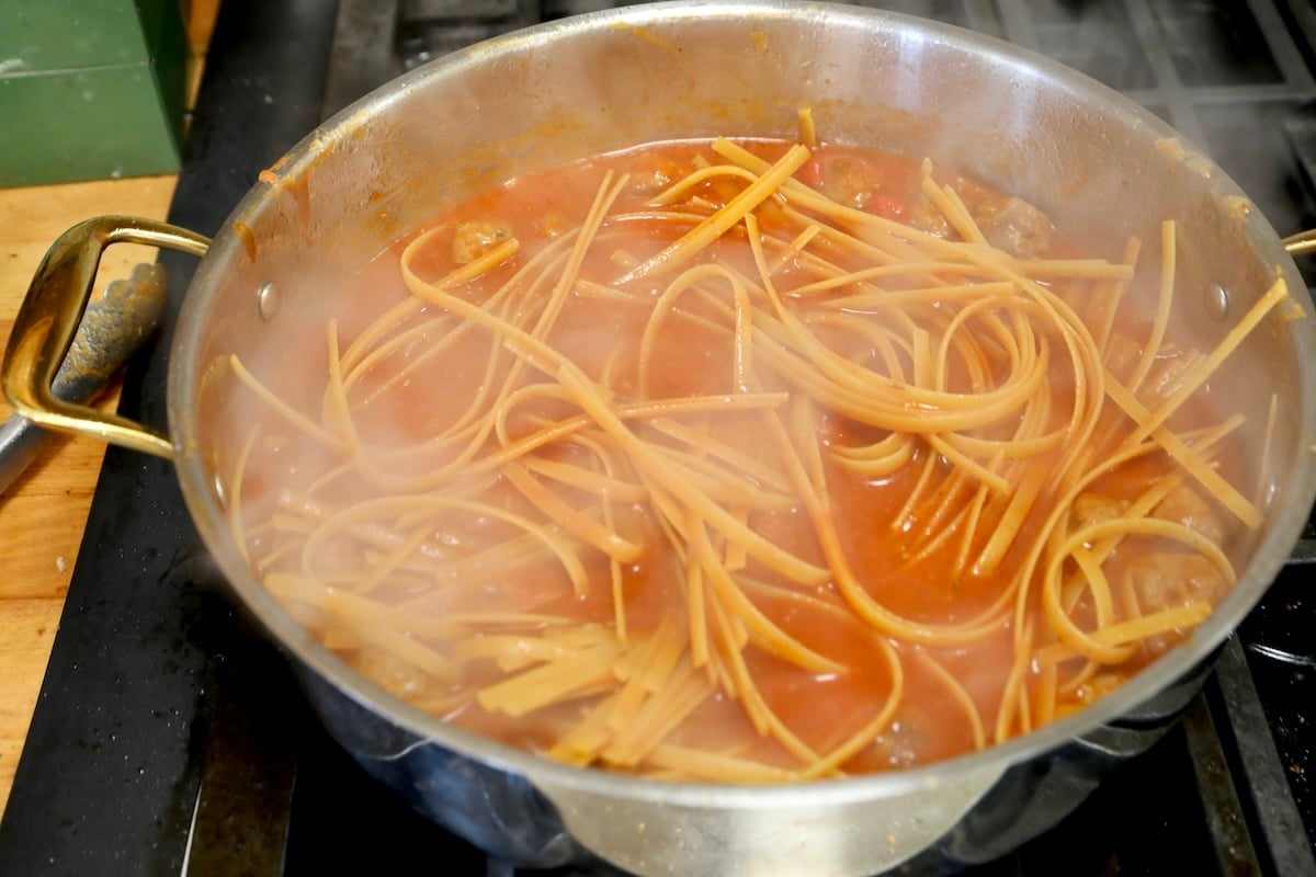 Cooking pasta and meatballs in a pan.