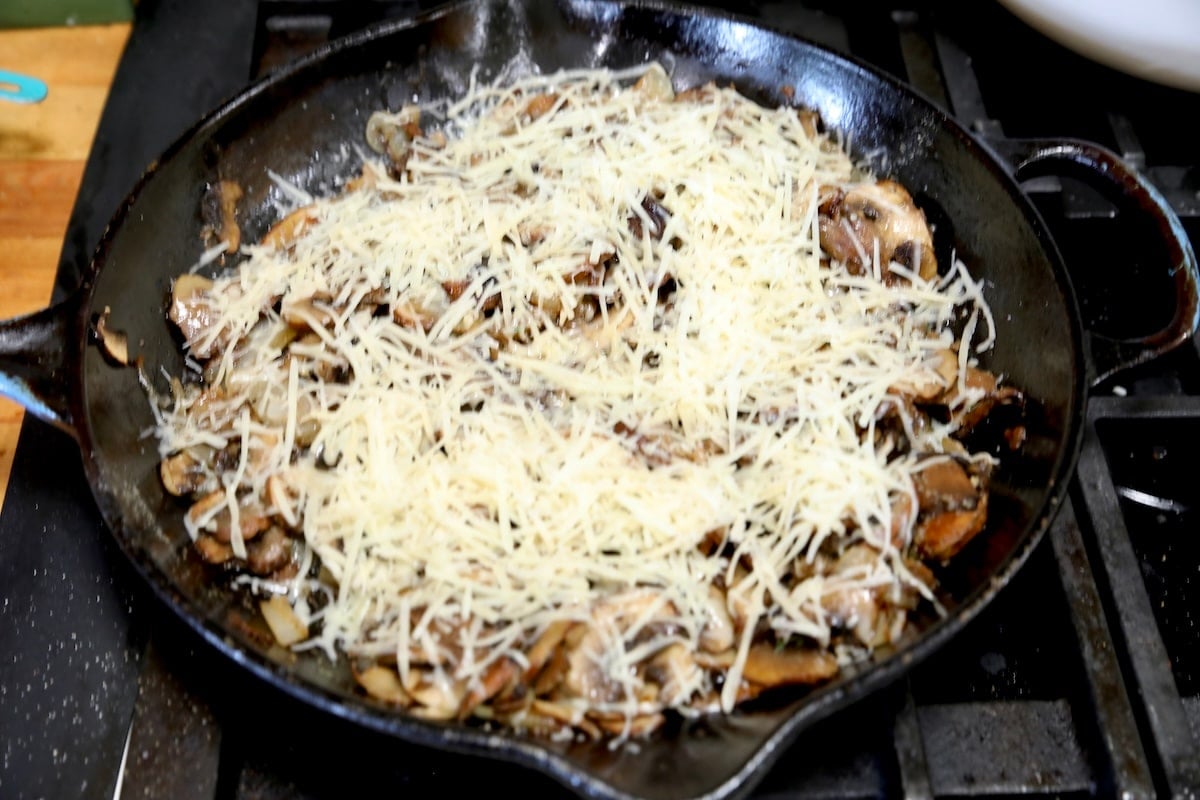 Grated cheese on top of mushrooms in a skillet.