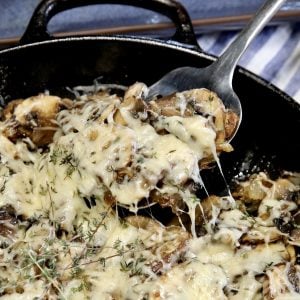 Sauteed mushrooms topped with Parmesan, spoon in skillet.