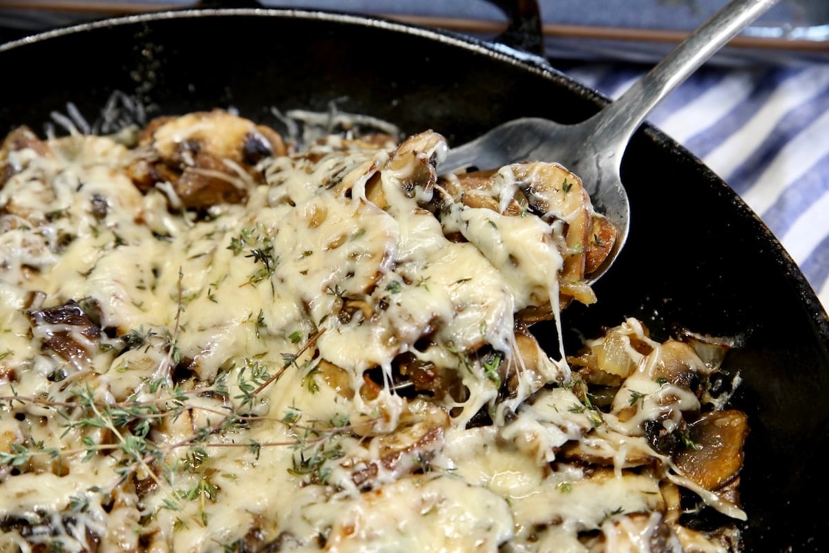 Mushrooms with melted parmesan cheese in a skillet with spoonful.