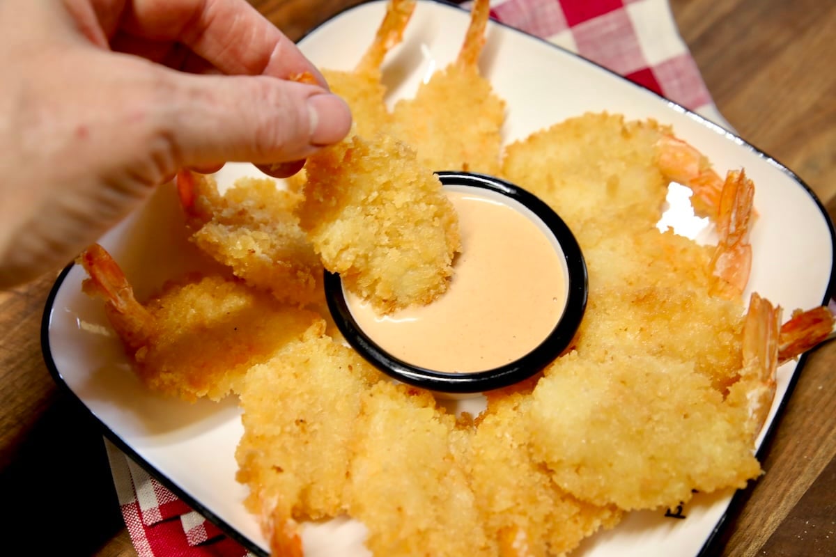 Hand held shrimp dipping in sauce cup.