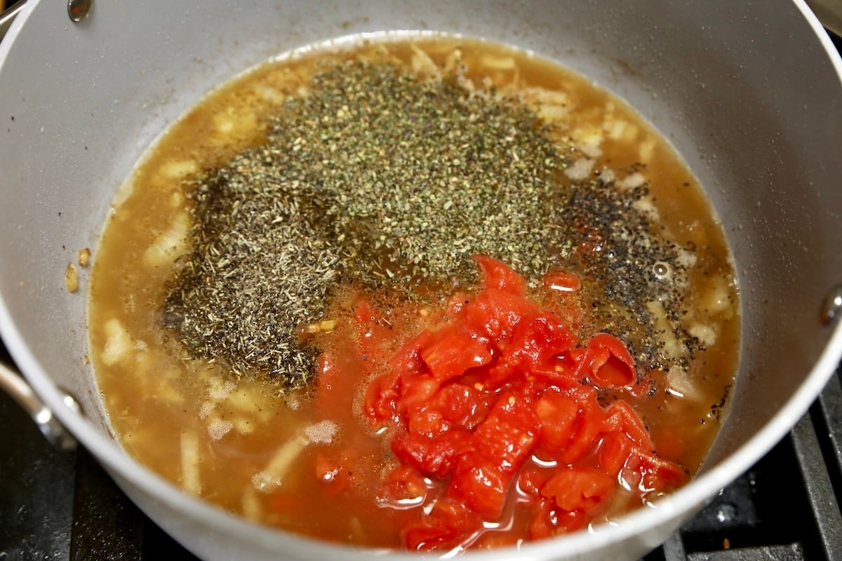 Making soup with tomatoes, chicken broth, herbs.