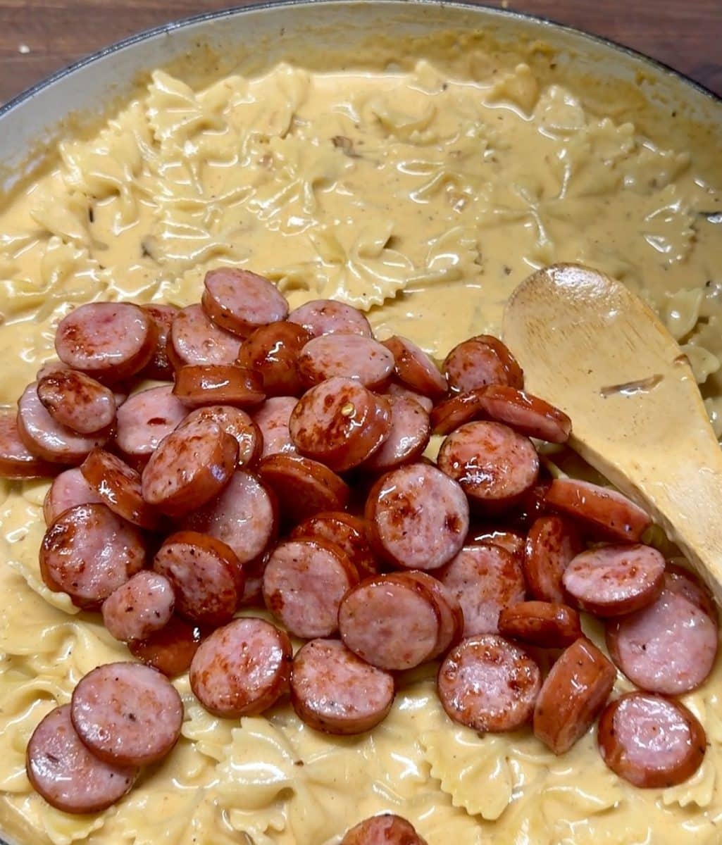 Stirring smoked sausage into cheddar pasta.